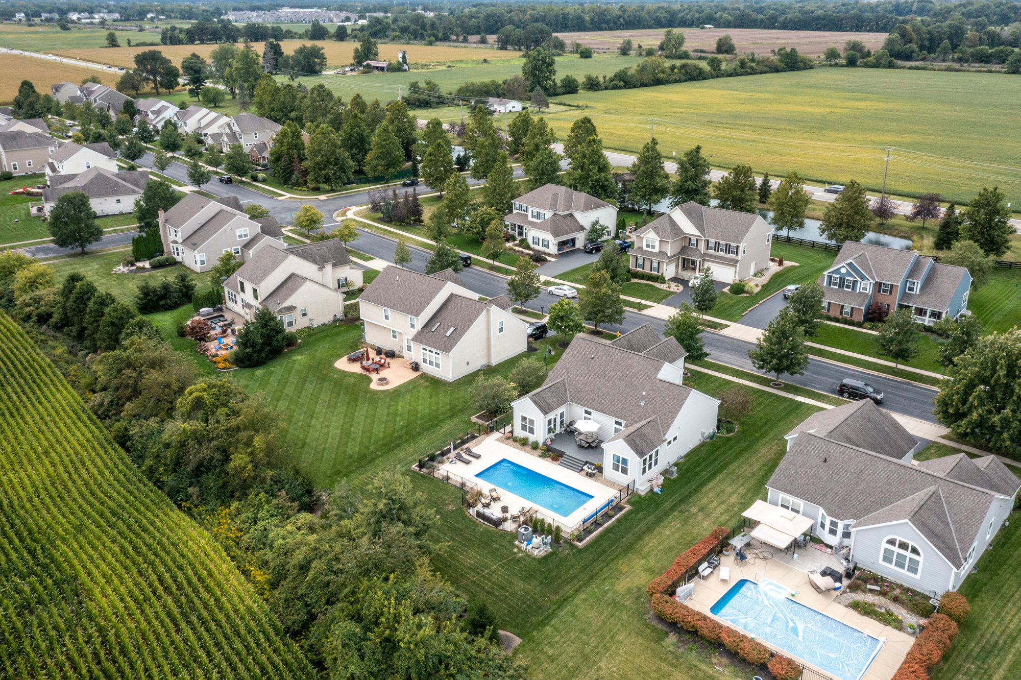 Aerial view of homes and swimming pools beside open fields